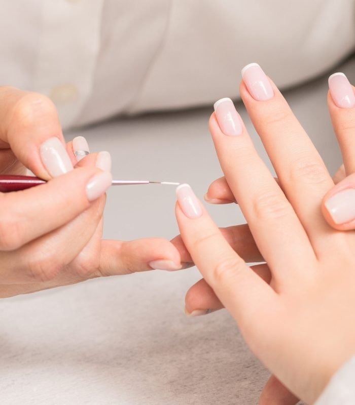 Hand of young woman receiving french manicure by beautician at nail salon.